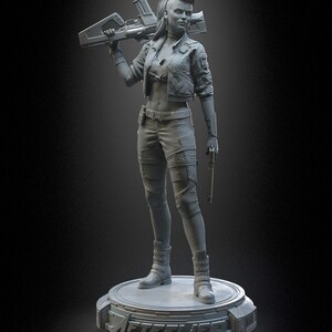 Pode incluir: Uma estatueta de resina cinza de um personagem com penteado moicano, vestindo uma jaqueta curta e cal&ccedil;as t&aacute;ticas, segurando um rifle grande sobre um ombro e uma pistola na outra m&atilde;o. A figura est&aacute; sobre uma base circular com a etiqueta AFTERLIFE.