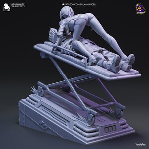 May include: A gray 3D-printed figurine depicting two figures on a medical stretcher. One figure is lying down, while the other is positioned above. The base of the stretcher has wheels and is set on a platform. The figurine is detailed and appears to be a collectible.