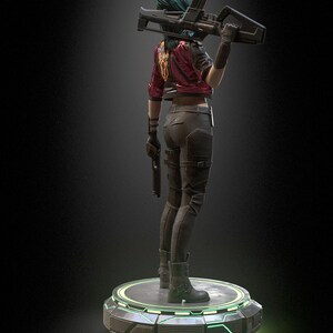 Pode incluir: Uma estatueta de um personagem com cabelo verde-azulado, vestindo uma jaqueta vermelha com um emblema amarelo, cal&ccedil;as escuras e botas. O personagem segura um rifle sobre o ombro e uma pistola na outra m&atilde;o, sobre uma base circular iluminada.