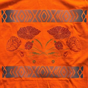 May include: Orange t-shirt with a blue and white geometric pattern and a floral design featuring red poppies.