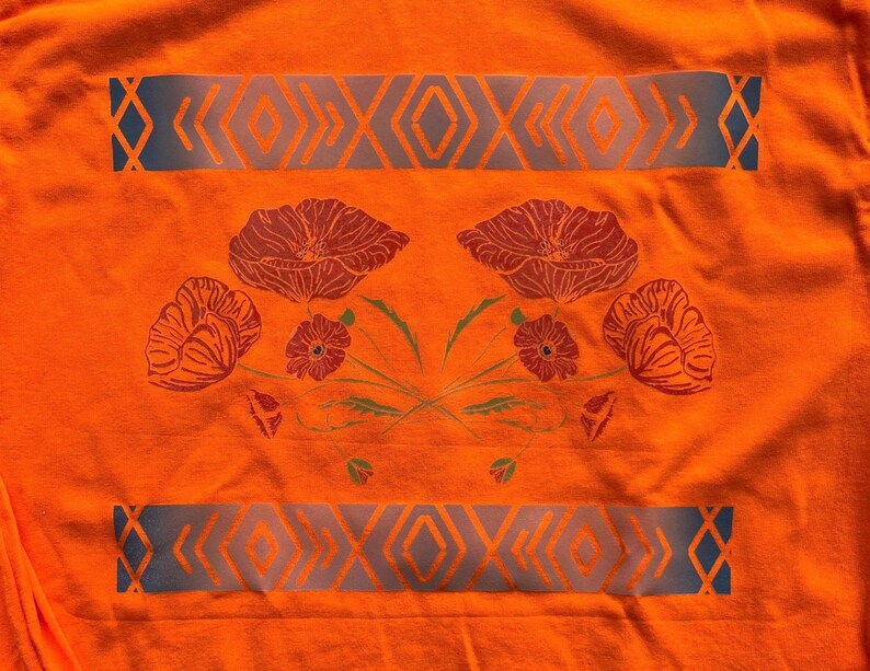 May include: Orange t-shirt with a blue and white geometric pattern and a floral design featuring red poppies.