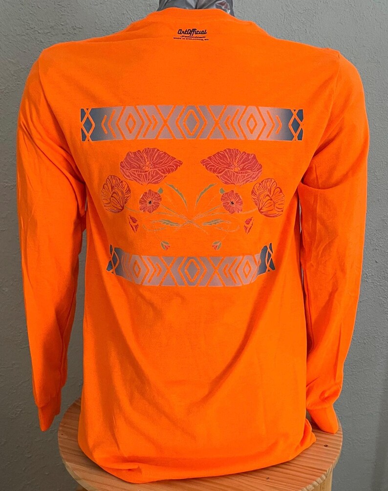 May include: Orange long-sleeve t-shirt with a geometric design and floral pattern on the back. The design features a gray and white geometric pattern with a floral pattern in shades of red, pink, and orange. The shirt has the text "Old/Faded" on the back.