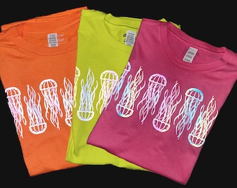 May include: Three t-shirts with a reflective iridescent jellyfish design. The shirts are orange, yellow, and pink.