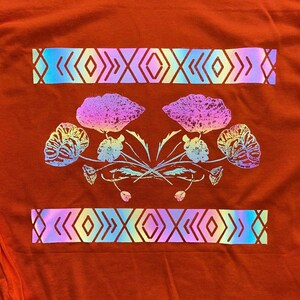 May include: A red t-shirt with a holographic design of flowers and geometric patterns. The flowers are pink, blue, and green, and the geometric patterns are blue, green, and purple.