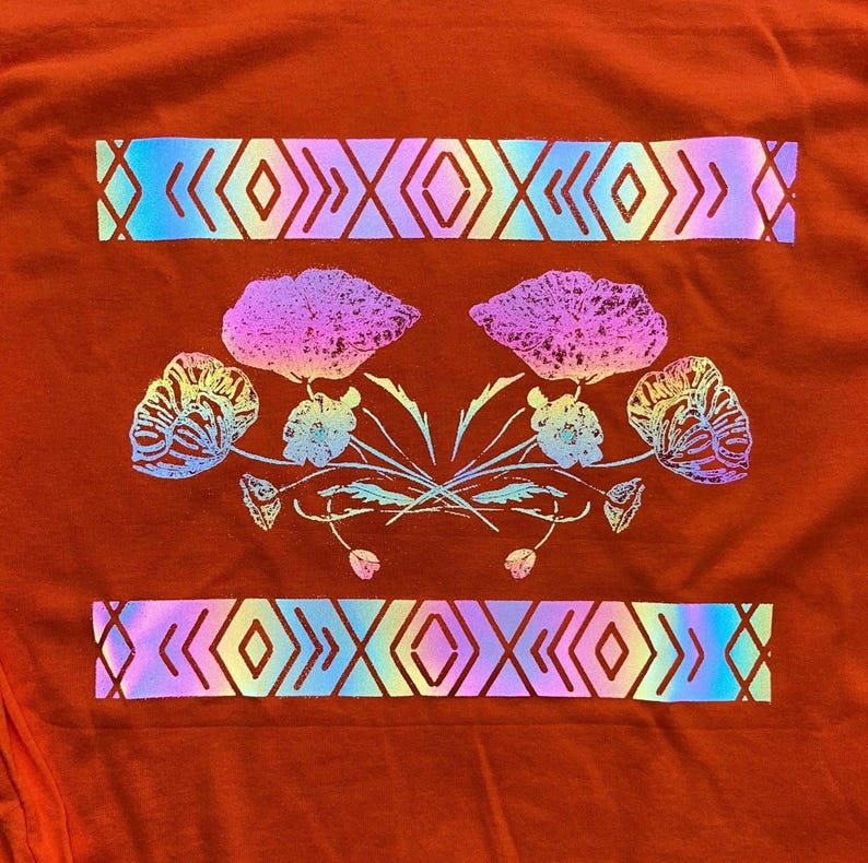 May include: A red t-shirt with a holographic design of flowers and geometric patterns. The flowers are pink, blue, and green, and the geometric patterns are blue, green, and purple.