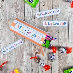 Puede incluir: Un cono de papel con forma de lápiz, rayas naranjas y el texto ABC - los geht's!, relleno de caramelos envueltos individualmente. Se incluyen tres etiquetas rectangulares de papel con texto colorido: Viel Spaß in der 1. Klasse!, Tollen Schulstart! y Hurra, endlich Schulkind!.