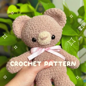 Puede incluir: Un oso de peluche tejido a crochet con una cinta rosa alrededor del cuello. El oso es marrón claro y tiene ojos negros. El texto "CROCHET PATTERN" está escrito en blanco sobre fondo negro. El texto "by @snailmail.studios" está escrito en negro sobre fondo blanco.