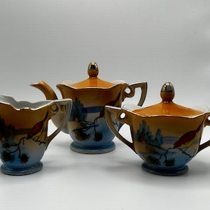 May include: A vintage porcelain tea set with a cream and blue floral design. The set includes a teapot, creamer, and sugar bowl with lids.