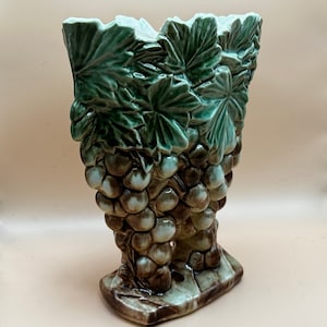 May include: A ceramic vase shaped like a bunch of grapes with green leaves. The vase is brown, green, and white.
