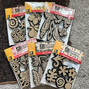 May include: A collection of decorative stamping cut paper sets. Each package features various shapes, including bows, flowers, and abstract designs. The stamps are black and tan, with colorful packaging.