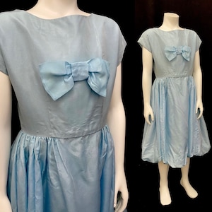 May include: A light blue dress with a large bow at the neckline. The dress has a fitted bodice and a full skirt.