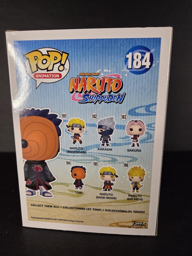 Pu&ograve; includere: Una scatola Funko Pop! Animation con personaggi di Naruto Shippuden. La scatola mostra immagini di Naruto, Kakashi, Sakura e Tobi. Il testo include "COLLEZIONALI TUTTI!" e il logo Funko. La scatola &egrave; numerata 184.