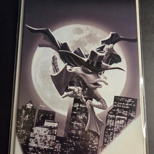 Może przedstawiać: Okładka komiksu w czerni i bieli z postacią w kapeluszu i pelerynie, na tle pełni księżyca. Postać leci nad miastem.