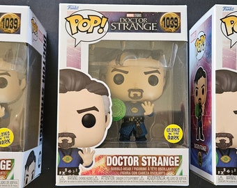 Può includere: Una statuetta in vinile Funko Pop! di Doctor Strange del film Doctor Strange dei Marvel Studios. La statuetta è vestita con un costume blu e verde e tiene un globo verde luminoso. La statuetta brilla al buio. La scatola è rossa, bianca e nera con il logo Funko Pop! e il logo dei Marvel Studios. La scatola riporta anche le parole "Doctor Strange" e "Glows in the Dark".