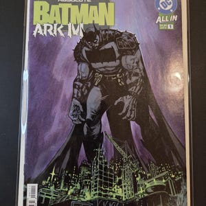 May include: A comic book titled Absolute Batman Arkham, issue number 1, featuring a large, dark-clad figure standing over a city skyline with construction cranes. The cover art uses a purple and black color palette with bold green text at the top.