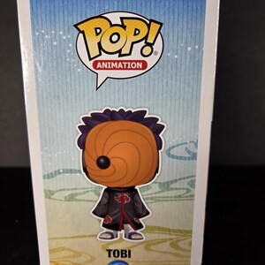 Pu&ograve; includere: Retro di una scatola Funko Pop! Animation con il personaggio Tobi. La scatola ha uno sfondo blu e giallo con il logo Pop! Animation. La figura di Tobi indossa un mantello nero con disegni di nuvole rosse e una maschera arancione. Il nome "TOBI" e il numero "184" sono stampati sotto.