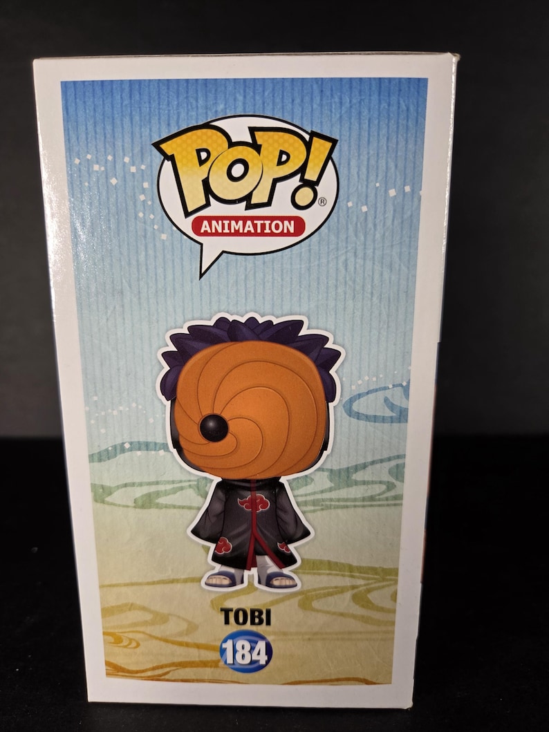 Pu&ograve; includere: Retro di una scatola Funko Pop! Animation con il personaggio Tobi. La scatola ha uno sfondo blu e giallo con il logo Pop! Animation. La figura di Tobi indossa un mantello nero con disegni di nuvole rosse e una maschera arancione. Il nome "TOBI" e il numero "184" sono stampati sotto.