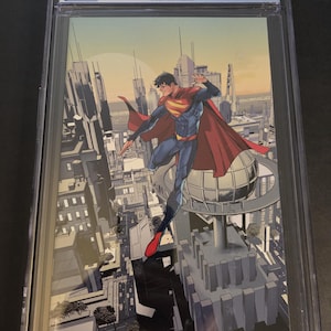 Op de afbeelding: Een beoordeeld stripboek met Superman: Son of Kal-El #1. De cover toont Superman in vlucht boven een stad. De strip is ingekapseld in een beschermende houder met een beoordeling van 9,8.