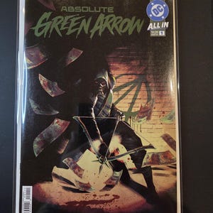 May include: A comic book titled Absolute Green Arrow All In number 1, featuring a hooded figure holding a bow and arrow amidst flying dollar bills against a dark brick wall background with a DC logo in the top right corner and a barcode at the bottom.