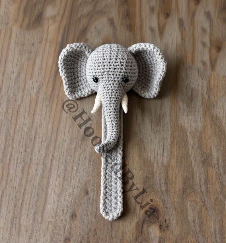 May include: A gray crocheted elephant toy with a long trunk and large ears. The elephant has black eyes and white tusks.