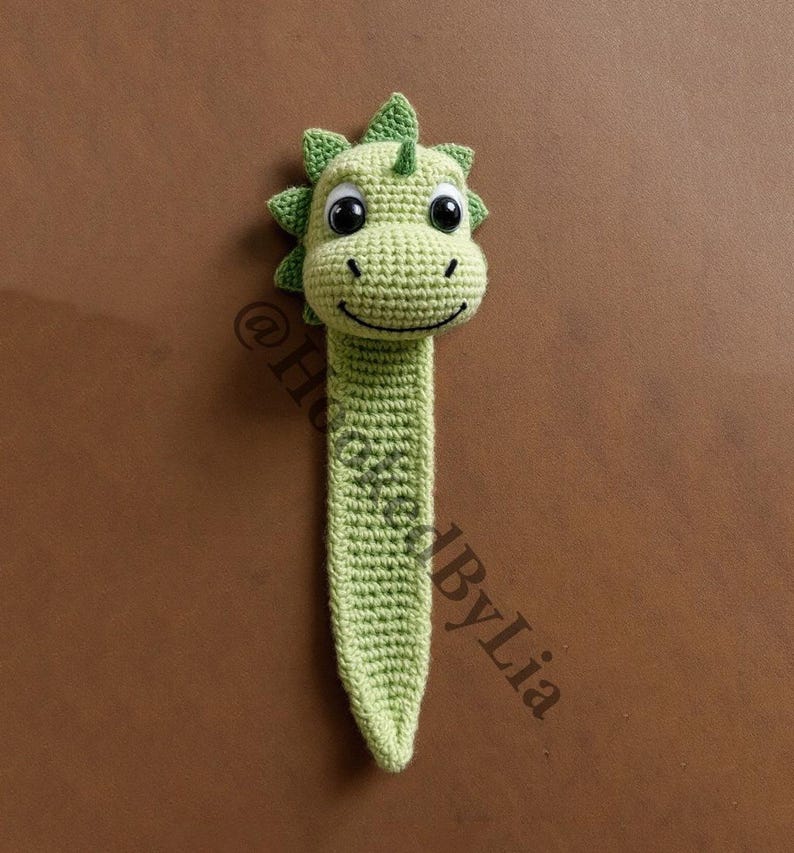 May include: Green crocheted dinosaur bookmark with black eyes and a smiling mouth.