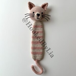 May include: A pink and white striped crocheted cat bookmark with black eyes and whiskers. The cat has a curled tail.