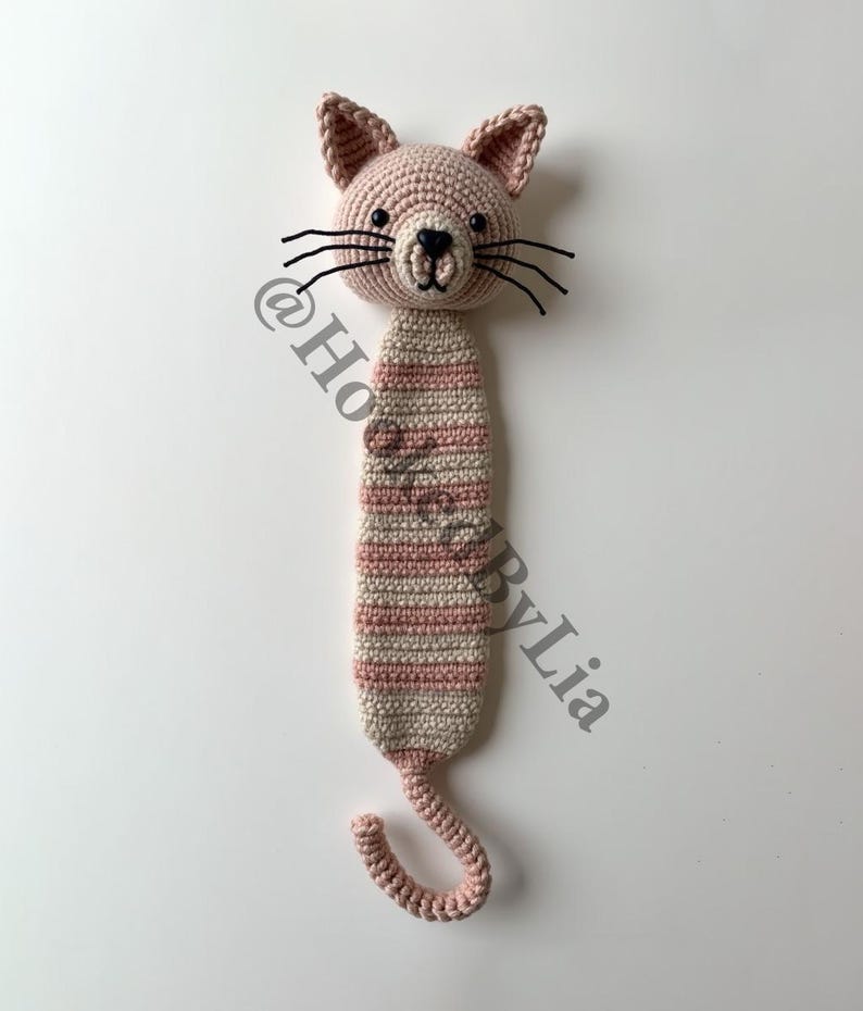 May include: A pink and white striped crocheted cat bookmark with black eyes and whiskers. The cat has a curled tail.