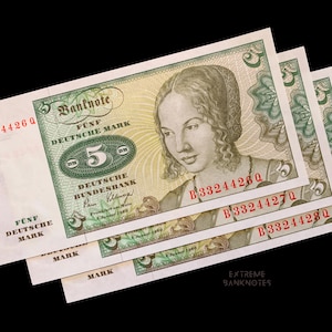 May include: Several vintage five Deutsche Mark banknotes are displayed against a black background. Each bill features a portrait of a woman and the text "FÜNF DEUTSCHE MARK". The serial numbers are visible in red. The banknotes are from January 2, 1980.