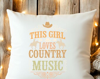 May include: White square pillow with the text "THIS GIRL LOVES COUNTRY MUSIC" in orange and green. The design includes a cowboy hat and silhouettes of horses. The pillow is on a wooden surface.
