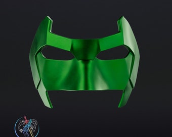 Può includere: Una maschera di supereroe in plastica verde con un design in rilievo testurizzato. La maschera ha una parte superiore appuntita e due fori per gli occhi.