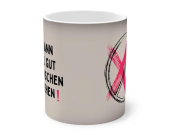 May include: A beige ceramic mug with black text that reads "Man kann ja gut kochen, wenn man es nicht tun muss!" and a pink X over a black circle.