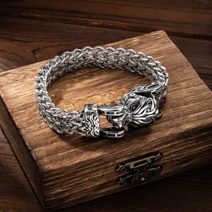 May include: A silver bracelet with a wolf head clasp. The bracelet is made of a braided chain design.