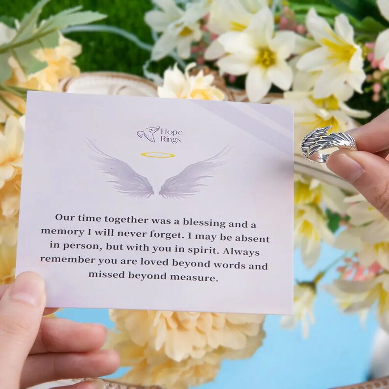 May include: A silver angel wing ring with a message card that reads "Our time together was a blessing and a memory I will never forget. I may be absent in person, but with you in spirit. Always remember you are loved beyond words and missed beyond measure." The card also has the words "Hope Rings" on it.