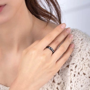 May include: A black ring with small, clear stones set into the band.