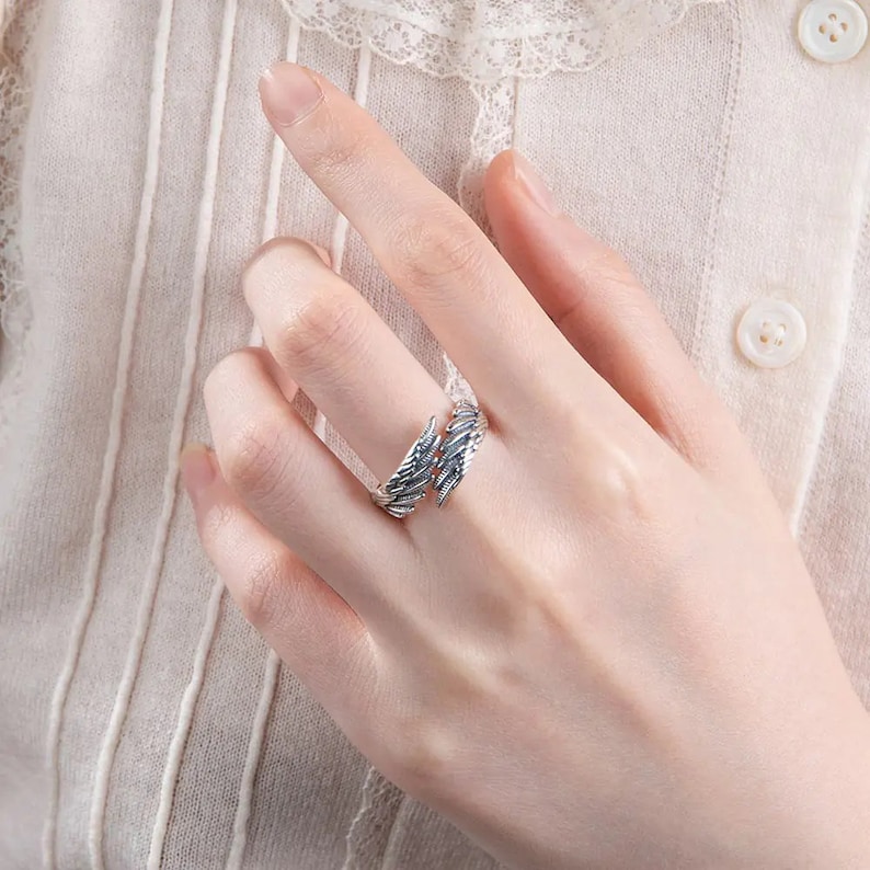 May include: A silver ring with a detailed wing design. The ring is open and adjustable to fit different finger sizes.
