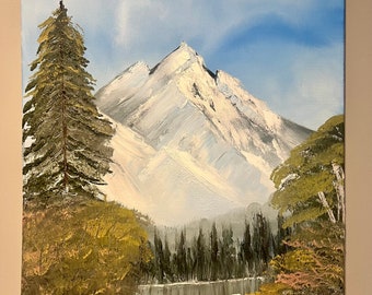 May include: A painting of a snow-capped mountain range with a lake in the foreground. The mountain is painted in shades of white and blue, with a few green trees in the foreground. The lake is a deep blue, with a reflection of the mountain in the water. The painting is signed "Kame 18" in the bottom right corner.