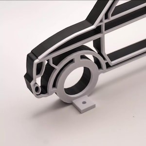 May include: A 3D-printed model of a car's side profile, featuring a black body with white accents and a gray wheel. The design is minimalist, showcasing the car's outline. A small, gray rectangular base supports the wheel.