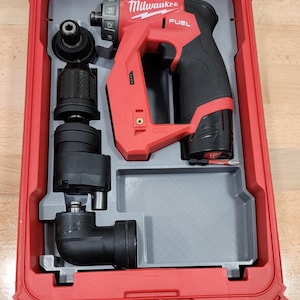 May include: A red and black Milwaukee FUEL power tool set in a red case. The set includes a drill, various attachments, and a storage compartment. The case is open, revealing the tools neatly organized inside.