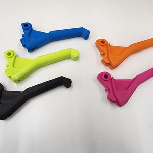 May include: Five 3D printed levers in different colors: blue, green, black, orange, and pink. The levers are designed for a motorcycle or bicycle.