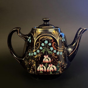 Peut inclure: Une théière noire avec des accents dorés et floraux. La théière a un design géométrique avec des accents bleus, roses et dorés. La théière est décorée d'un motif floral.