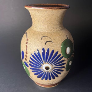 Puede incluir: Un jarrón de cerámica marrón con un diseño floral azul y verde. El jarrón tiene una base ancha y un cuello estrecho.
