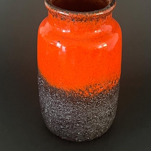 Op de afbeelding: Een cilindrische keramische vaas met een getextureerde, donkergrijze onderste helft en een feloranje bovenste helft. De rand is donkerder bruin. Deze decoratieve vaas is geschikt voor het presenteren van bloemen of als een op zichzelf staand kunstwerk.