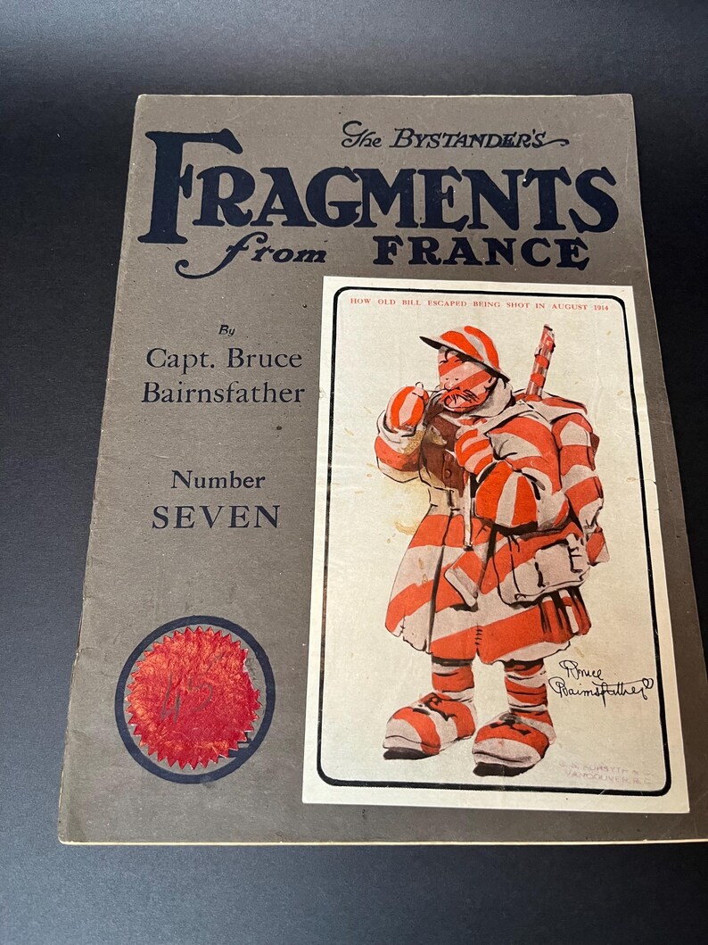 K&ouml;nnte beinhalten: Ein Vintage-Buchcover mit dem Titel "Fragments from France" von Capt. Bruce Bairnsfather. Das Cover ist grau mit dunkelblauem Text und einem roten Siegel. Eine gerahmte Illustration zeigt eine Cartoonfigur in rot-wei&szlig;en Streifen.