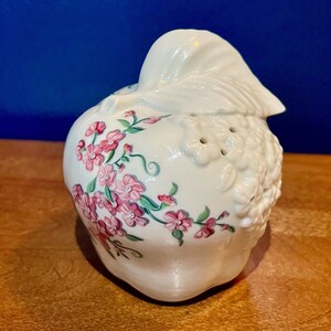 May include: White ceramic apple shaped kitchen decor with pink floral design and a textured top.