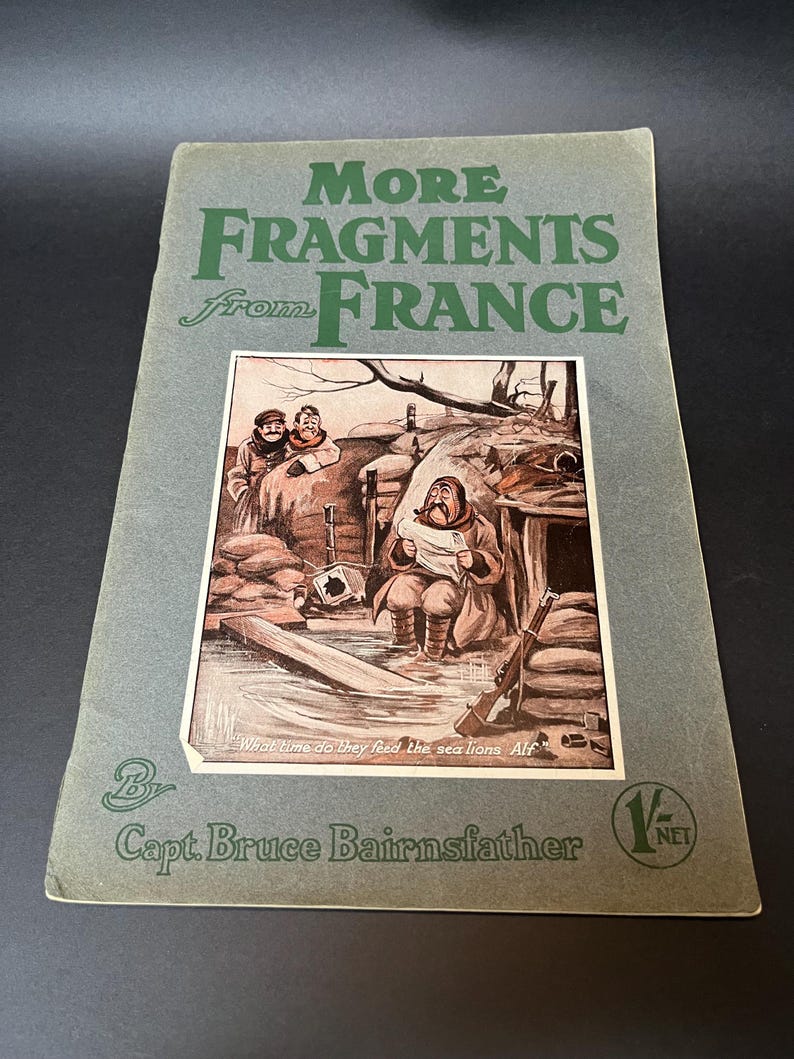 K&ouml;nnte beinhalten: Ein Vintage-Buchcover mit dem Titel "More Fragments from France" von Capt. Bruce Bairnsfather. Das Cover ist in ged&auml;mpftem Gr&uuml;n gehalten, der Titel in gro&szlig;en gr&uuml;nen Buchstaben. Die Illustration zeigt Soldaten in einem Sch&uuml;tzengraben, mit dem Text "What time do they feed the sea lions Alf?"