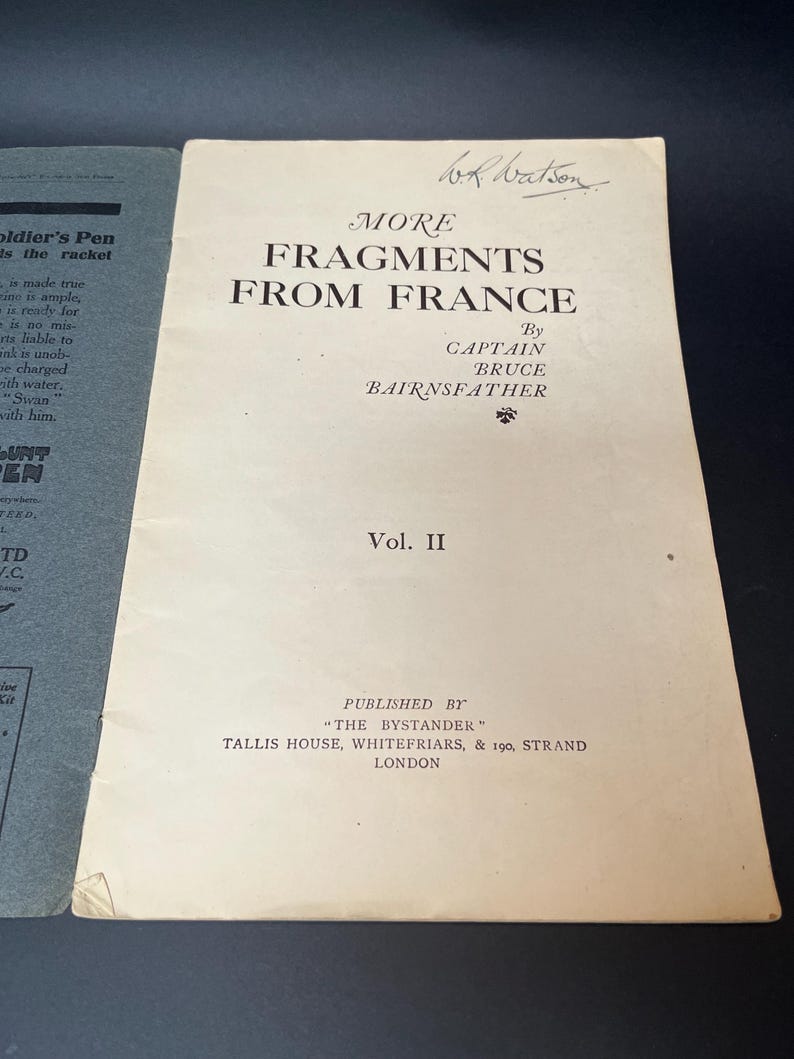 K&ouml;nnte beinhalten: Ein Vintage-Buchcover mit dem Titel "MORE FRAGMENTS FROM FRANCE" von Captain Bruce Bairnsfather. Das Cover ist cremefarben mit schwarzem Text und einer handschriftlichen Signatur. Das Buch ist Band II, herausgegeben von "The Bystander" in London.