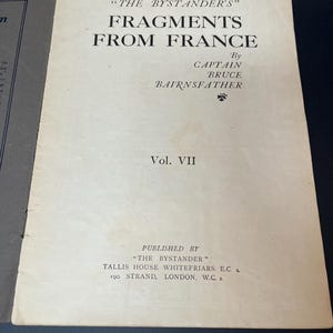 K&ouml;nnte beinhalten: Aufgeschlagenes Buch mit dem Titel "FRAGMENTS FROM FRANCE" von Captain Bruce Bairnsfather. Das Cover ist cremefarben mit schwarzem Text. Das Buch ist Band VII, herausgegeben von "THE BYSTANDER" in London.