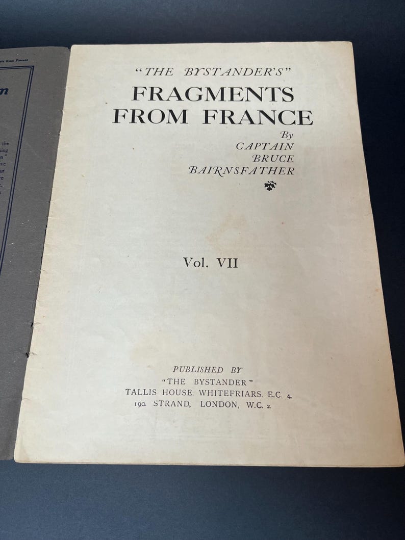 K&ouml;nnte beinhalten: Aufgeschlagenes Buch mit dem Titel "FRAGMENTS FROM FRANCE" von Captain Bruce Bairnsfather. Das Cover ist cremefarben mit schwarzem Text. Das Buch ist Band VII, herausgegeben von "THE BYSTANDER" in London.