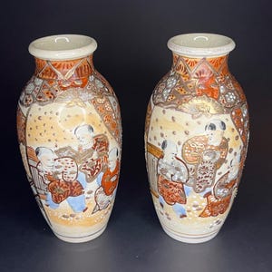 May include: Pair of vintage ceramic vases with a cream background and colorful floral and geometric patterns. The vases feature a scene of people in traditional clothing.