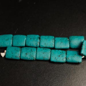 Peut inclure: Un brin de perles rectangulaires bleu turquoise avec un motif moucheté. Les perles sont enfilées sur un cordon blanc.
